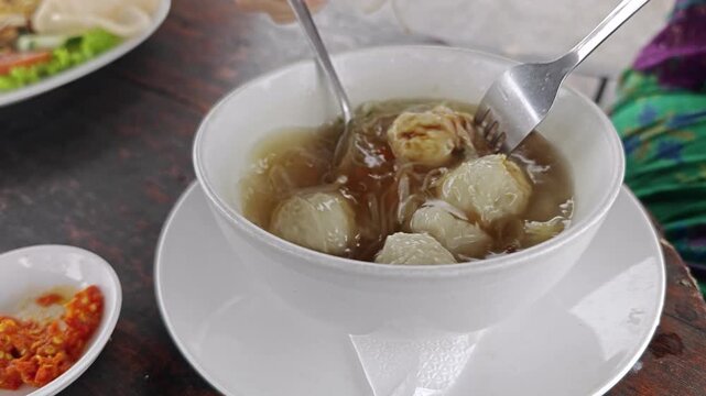 Mixing Sweet Soy Sauce into Indonesian Tekwan Fish Ball Soup with Spoon and Fork