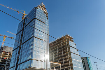 Modern office skyscrapers under construction in Belgrade, Serbia, with glass facades, cranes,...