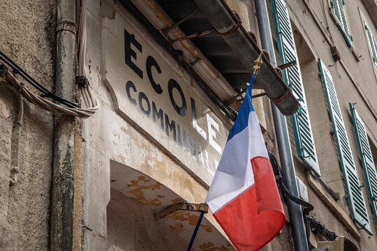 French flag hanging in front of an ecole communale, meaning primary school in french, in France, showing signage linked to local public education and the school system.