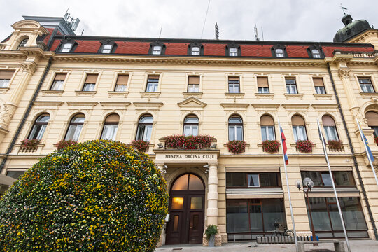 Facade of Mestna Obcina Celje, meaning municipality of celje in slovenian, the city hall and local administration headquarters of Celje, Slovenia, flags, historic architecture, and municipal entrance.