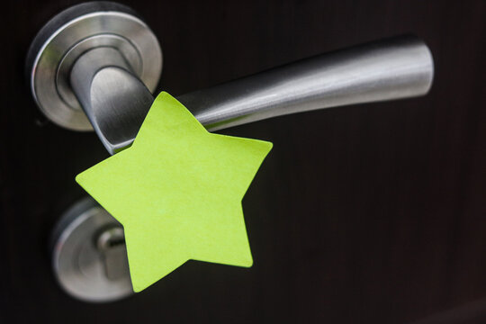 A bright green star-shaped sticky note attached to a metallic silver door handle.