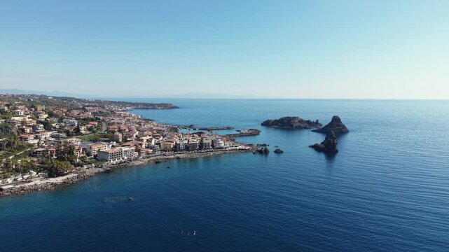 Aerial view of the Islands of the Cyclops and the coastal town of Aci Castello with volcanic rock formations in the blue Mediterranean sea, Aci Castello, Catania, Italy.