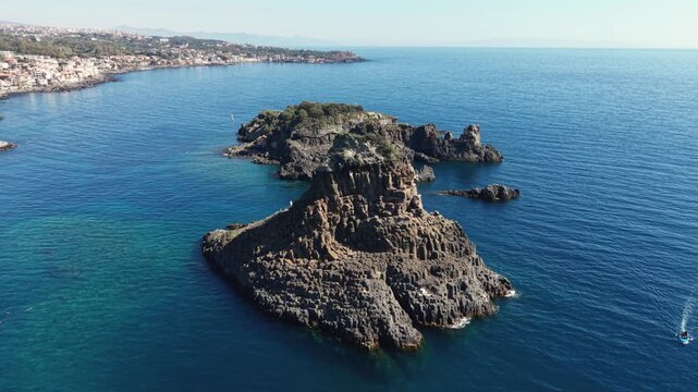 Aerial view of the Islands of the Cyclops featuring volcanic rock formations and clear blue water along the coastline of Aci Castello, Citta metropolitana di Catania, Italy.