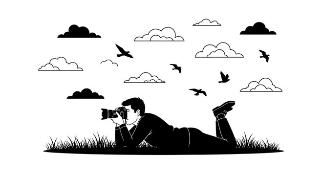 A silhouette of a photographer lying on the grass capturing images with a camera.