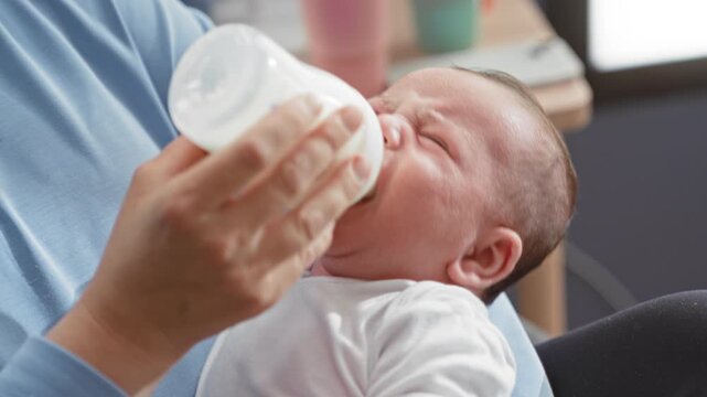 Baby boy feeding from a bottle with mouth latched while held on a home lap in a living room; bonding comfort.