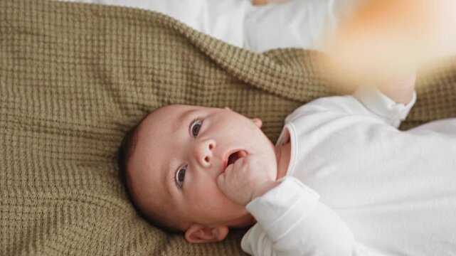 Boy sucking from bottle with adult hand holding nipple while lying on bed in a bedroom; gentle comfort.