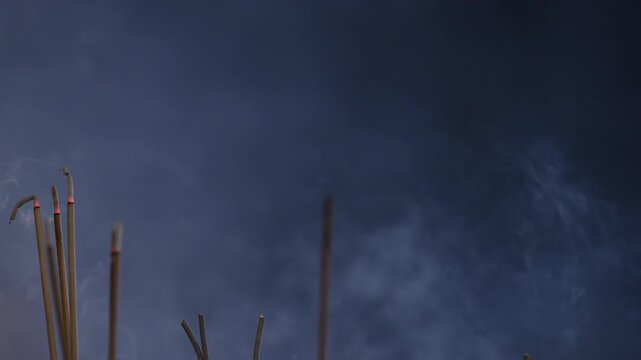 incense smoke rising slowly during night ritual against dark night sky background overlay. Continuous vertical flow of white smoky texture with close up sharp focus on burning joss stick embers.