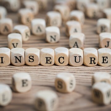 Conceptual representation of profound insecurity with wooden letter blocks forming the word 'INSECURE', highlighting emotional vulnerability, anxiety, and self-doubt on a rustic textured surface