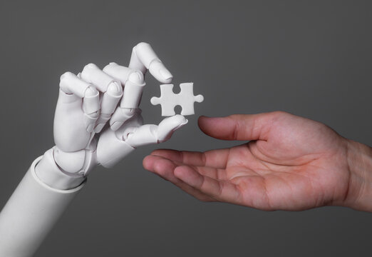 Robot hand passing a jigsaw puzzle piece to a human hand.