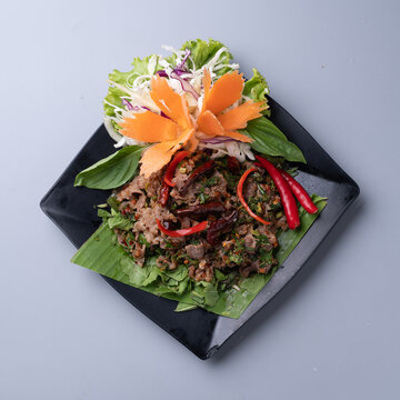 Thai spicy minced beef salad with herbs and chili on black plate.