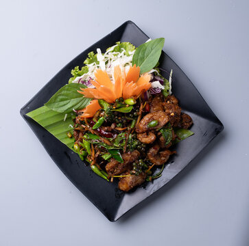 Stir fried spicy fish with herbs and peppercorns on black plate.