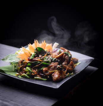 Stir fried spicy fish with herbs and peppercorns on black plate.