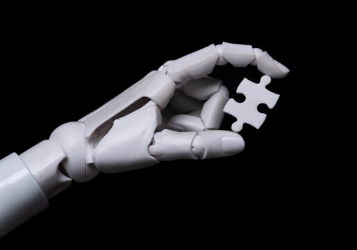 Robotic hand holding single white puzzle piece on black background.