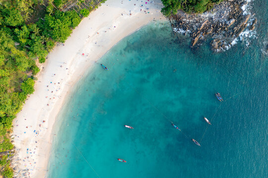 People relax on the white sand beach and swim in the clear blue ocean water beside lush jungle on Patong Beach, Phuket, Thailand during vacation