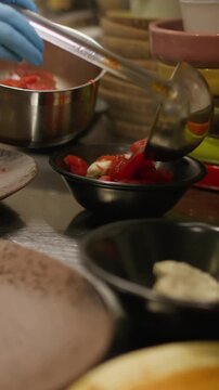 Vertical video. Ladling food. Portioned dish. Chef pouring hot red liquid meal in bowls standing row. Serving borsch on restaurant kitchen interior .