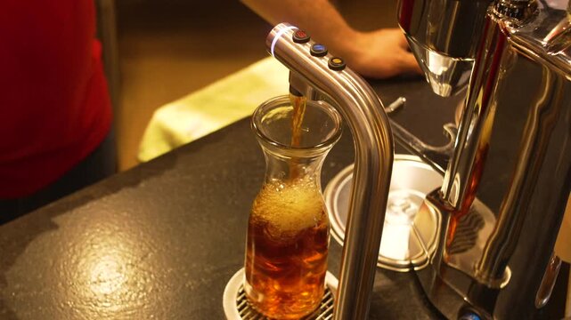 Stainless Steel Specialty Coffee Dispenser Filling Glass Carafe with Iced Coffee at Modern Cafe Bar, Barista Equipment