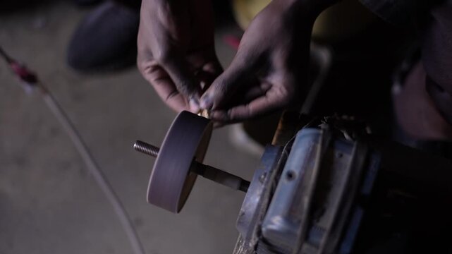 A skilled artisan grinding and polishing a brass ornament in his hand using a rotating machine in a workshop. Traditional metal craftsmanship and a handmade production process.