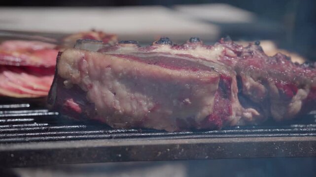 Close-up of juicy beef short ribs slow cooking over a wood-fired grill with smoke and glowing heat as the barbecue lid closes to create an oven-style cooking process.