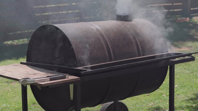 Traditional outdoor parrilla with the lid closed to oven-cook asado over a wood fire. Dense wood smoke surrounds the rustic barbecue grill during slow cooking.