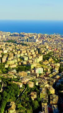 Vertical video. Genoa, Italy. Drone footage of the historic port city, dense urban hillsides descending toward the Ligurian Sea with ships and harbor infrastructure visible along the waterfront. Dron