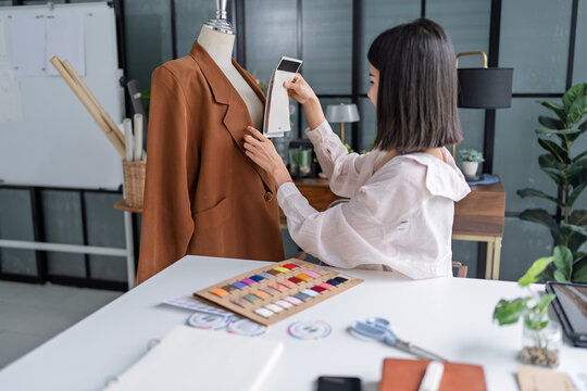 Asian woman designer selecting fabric samples while creating fashion collection in creative studio