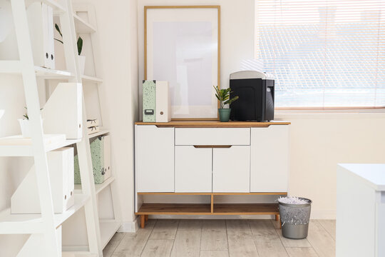 Shredder with blank frame and folders on chest of drawers in light office