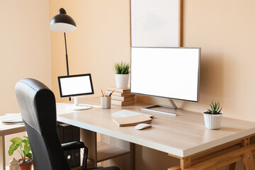 Fototapeta premium Modern workplace with blank computer monitor and plants near beige wall in office