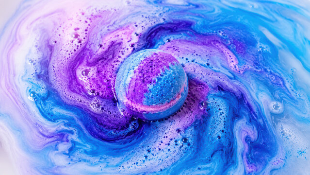 Bright blue and purple bath bomb dissolving in water creating a beautiful swirling colorful pattern