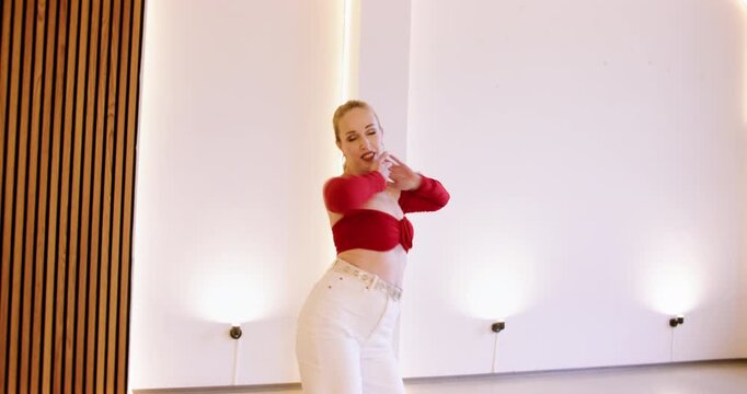 Latin dance instructor. Sensual flexibility. Beautiful woman in bright top moving bending body stepping rhyme indoors in light studio.