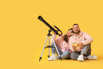 Obraz premium Young couple with notebook and telescope sitting on yellow background