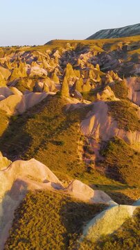 Vertical video. Goreme, Nevsehir, Turkey. Devrent Valley surreal rock sculptures and fantasy-like formations, aerial drone view in warm golden sunset light over eroded terrain. Aerial View. Rich colo