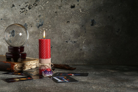 Magical crystal ball with tarot cards, book and wax candle on grunge grey background