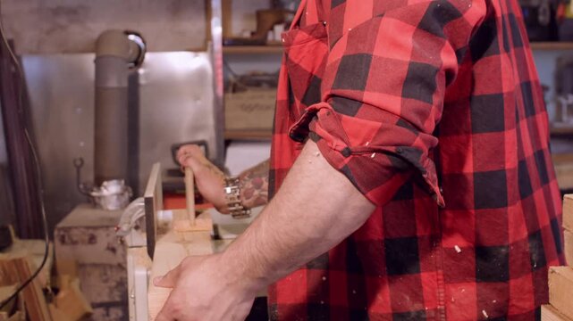 Carpentry occupation. Furniture making. Craftsman with ear protectors smoothing wood on thickness planer. Saw dust flying in industry interior.
