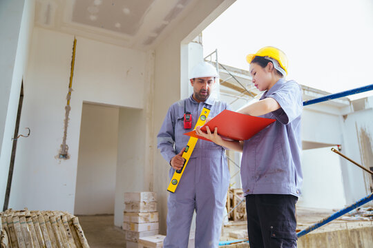 Male and female builders with hard hats and spirit level checking blueprints