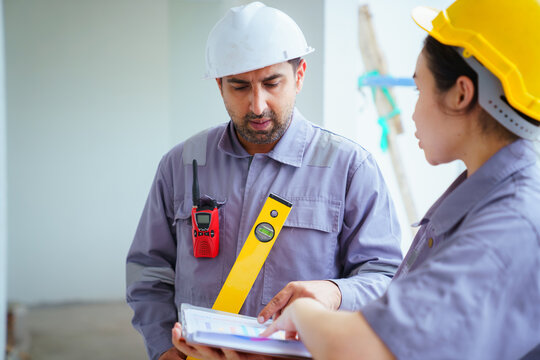 Male and female builders with hard hats and spirit level checking blueprints