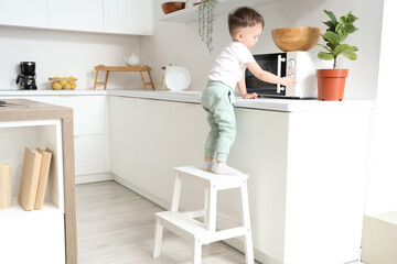 Little boy on step stool near microwave oven in kitchen. Child at risk © Pixel-Shot