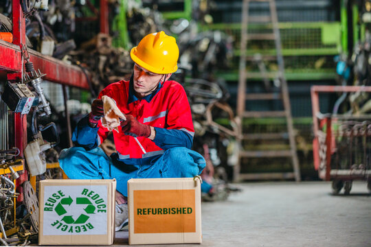 Male technician inspecting used auto parts for refurbishing and recycling in scrapyard
