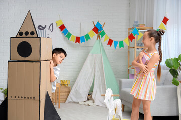 Naklejka premium Cute little children with adventure book and cardboard rocket at home