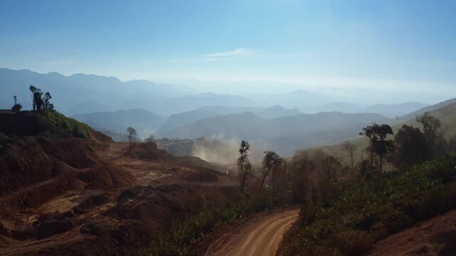 Top-down aerial tracking shot of an active iron ore mine, Red laterite soil and mining equipment contrast with surrounding green forest and mountains in Xieng Khouang province, Lao PDR.