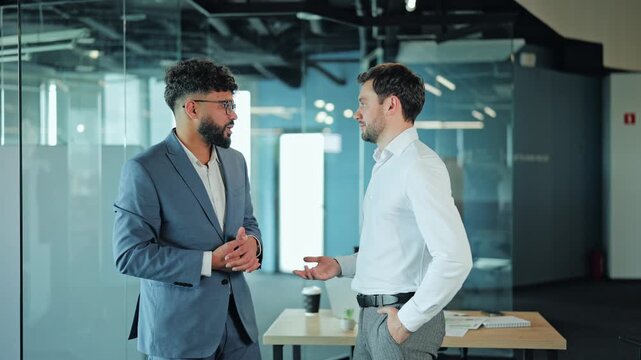 Successful corporate professionals having conversation standing in contemporary workspace. Colleague in suit and manager in white shirt discussing company strategy or project details.