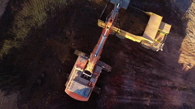 Top-down aerial tracking shot of an active iron ore mine, Red laterite soil and mining equipment contrast with surrounding green forest and mountains in Xieng Khouang province, Lao PDR.
