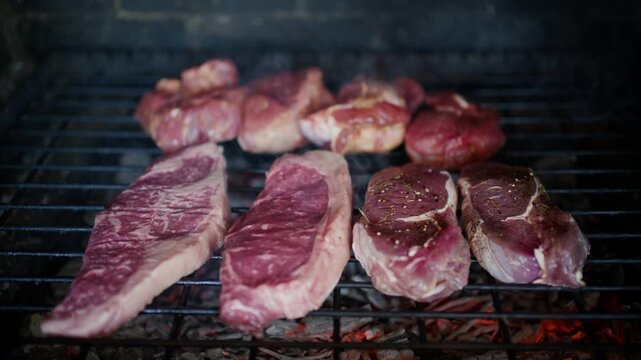 Raw sirloin steaks and marinated meat cuts grilling over hot charcoal embers.