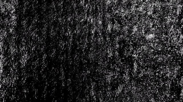 Dark rough textured surface resembling weathered stone, featuring vertical streaks and granular details.