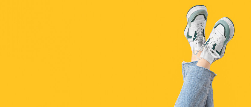 Female legs in stylish sneakers and jeans on yellow background
