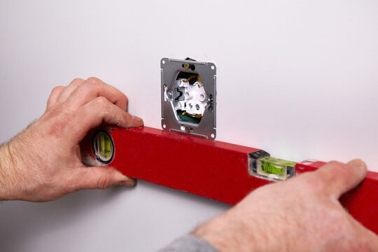 Work on installing electrical sockets. An electrician uses a building level to check that the sockets are level