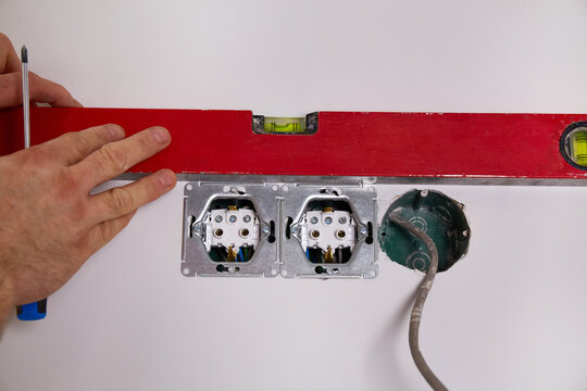 Work on installing electrical sockets. An electrician uses a building level to check that the sockets are level