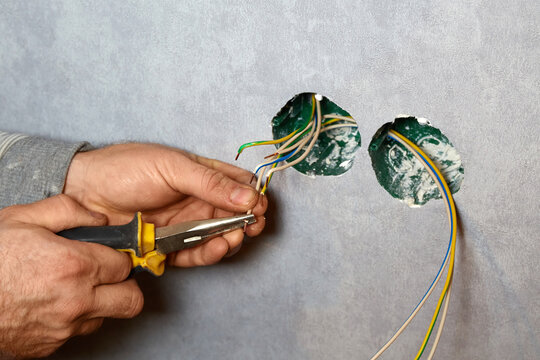 Electrician cutting and preparing electrical wires with pliers for installation.