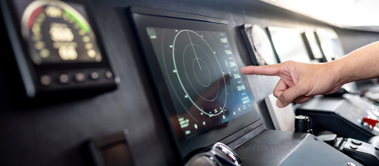 Captain hand pointing at marine radar monitor screen or GPS navigation map on boat dashboard. Nautical vessel control system in wheelhouse or ship bridge. Modern boating technology and operation © zephyr_p