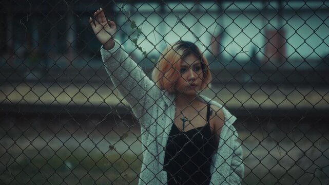 Young woman standing behind chain-link fence in urban industrial setting
