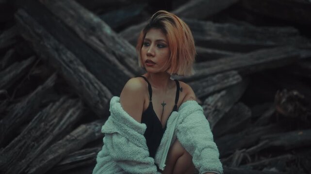 Young woman crouching on weathered driftwood in moody overcast light
